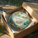 A decorative ornament in a box, featuring a tropical scene with a lighthouse, palm trees, and colorful marine life.