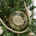 A circular ornament hanging on a Christmas tree, featuring a scenic landscape with a lake, trees, and a cabin.
