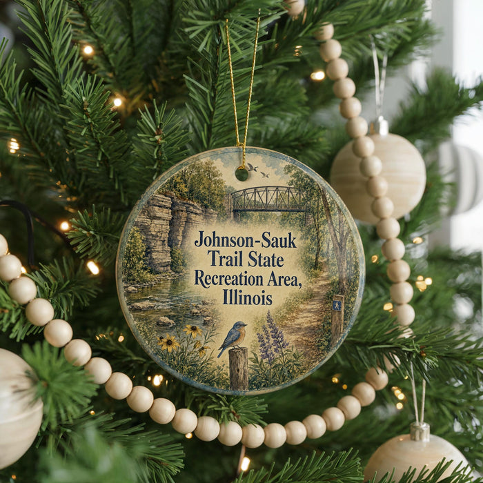A round ornament hanging on a Christmas tree, featuring a scenic image of a trail in the Johnson-Sauk Trail State Recreation Area, Illinois.