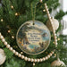 A round ornament hanging on a Christmas tree, featuring a scenic landscape with a waterfall and mountains.