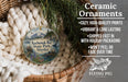 Ceramic ornaments, featuring a bird and a landscape, are displayed in a basket with pine branches.