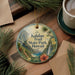 A circular ornament with a tropical landscape design, featuring palm trees, flowers, and a waterfall, hangs on a wooden surface.
