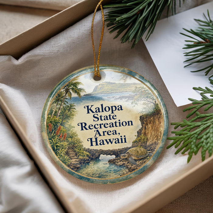 A circular ornament with a tropical landscape design, featuring palm trees, a waterfall, and a bird, is displayed in a box with pine branches.