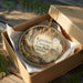 A circular ornament with a scenic image of the Kachner Caves in Arizona, displayed in a wooden box with a gold string.