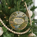 A circular ornament hanging on a Christmas tree, featuring a scenic landscape with a river, trees, and a city skyline in the background.