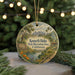 A circular ornament with a painting of a scenic landscape, featuring a city skyline in the background and a path leading to a body of water.