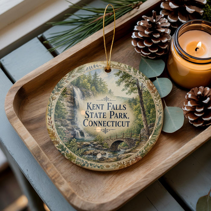 A wooden tray with a decorative ornament featuring a scenic image of Kent Falls State Park in Connecticut, accompanied by pine cones and a lit candle.