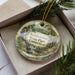 A decorative ornament in a box, featuring a scenic landscape with trees and a waterfall, with the text "Ketletown State Park, Connecticut" printed on it.