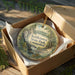 A decorative ornament in a box, featuring a scenic landscape with a waterfall and trees, with the text "Kettleton State Park, Connecticut" printed on it.