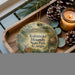 A wooden tray with a decorative ornament featuring a deer and a pond, surrounded by pine cones and a lit candle.