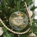 A round ornament hanging on a Christmas tree, featuring a scenic landscape with a bridge, trees, and a deer.
