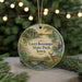 A round ornament with a scenic landscape featuring a river, bridge, and deer, hanging from a string.