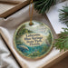 A decorative ornament with a tropical scene, featuring palm trees, a bird, and a water body, is displayed in a box with pine branches.
