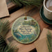 A circular ornament with a tropical scene depicting a manatee and palm trees, surrounded by greenery, hangs on a wooden surface.