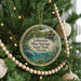 A round ornament hanging on a Christmas tree, featuring a scenic image of a manatee and a house surrounded by palm trees.