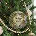 A round ornament hanging on a Christmas tree, featuring a scenic landscape with a lake, trees, and a cabin.
