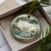 A decorative ornament with a scenic landscape of Lake Cascade State Park, Idaho, featuring a cabin, mountains, and a bird of prey.