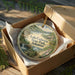 A decorative ornament in a box, featuring a scenic landscape with a lake, trees, and a waterfall.