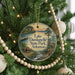 A circular ornament hanging on a Christmas tree, featuring a scenic landscape with a lake, forest, and mountains.