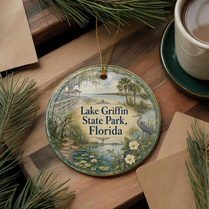 A decorative ornament featuring a scenic view of Lake Griffin State Park in Florida, surrounded by pine branches and a cup of coffee.