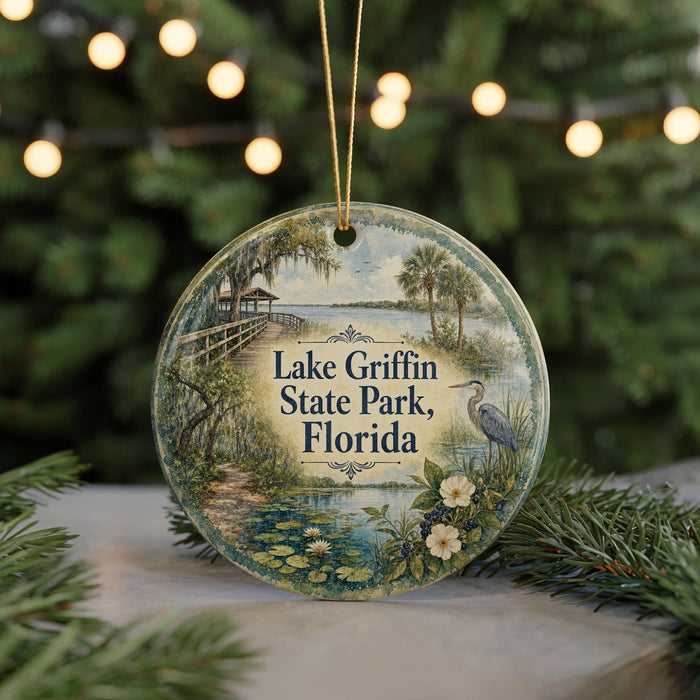 A round ornament with a painting of Lake Griffin State Park, Florida, featuring a bird, palm trees, and a wooden walkway.