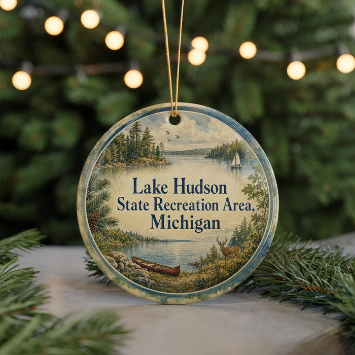 A round ornament with a scenic lake and forest landscape, featuring a boat and a deer, is displayed in front of a blurred background with Christmas lights.