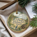 A round ornament with a bird and a turtle, surrounded by greenery, is displayed in a box.