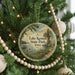 A circular ornament hanging on a Christmas tree, featuring a scenic landscape with a lake, trees, and a path.