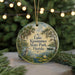 A round ornament with a painting of a lake, palm trees, and a bird, hanging on a string.