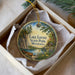 A decorative ornament in a box, featuring a scenic landscape with a lake, trees, and a cabin, along with the text "Lake Louise State Park, Minnesota".