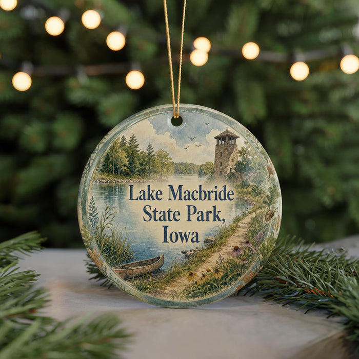 A round ornament with a scenic image of Lake Macbride State Park, Iowa, featuring a lake, a tower, and a path surrounded by trees and flowers.