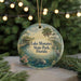 A circular ornament with a painting of a lake, palm trees, and a bird, hanging on a string.