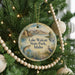 A round ornament hanging on a Christmas tree, featuring a scenic landscape with mountains, a lake, and wildlife.