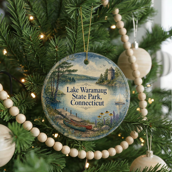 A round ornament hanging on a Christmas tree, featuring a scenic landscape with a lake, trees, and a boat.