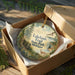 A round ornament in a box, featuring a scenic image of Lakelands Trail State Park in Michigan.