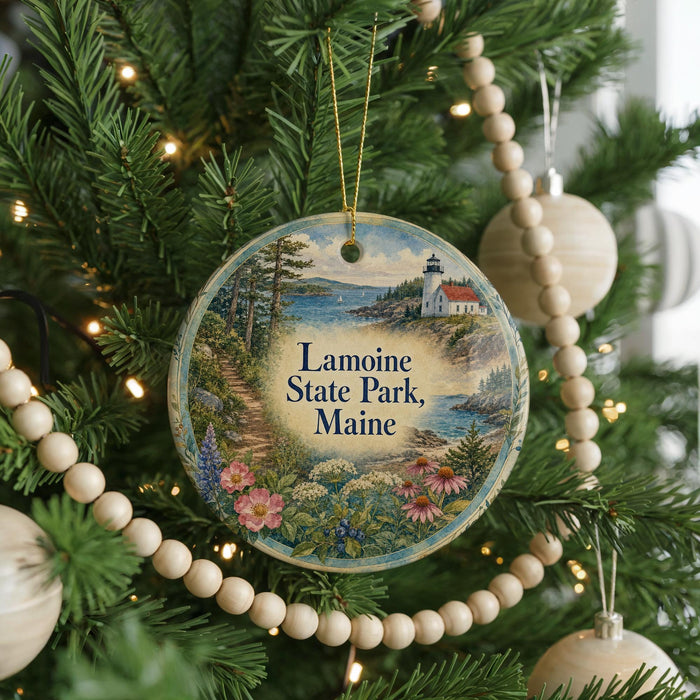 A round ornament hanging on a Christmas tree, featuring a scenic landscape with a lighthouse and a path leading through the woods.