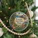 A round ornament hanging on a Christmas tree, featuring a scenic landscape with a lighthouse and a path leading through the woods.