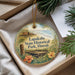 A decorative ornament with a tropical island scene and text, placed in a box with pine branches.
