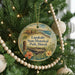 A round ornament hanging on a Christmas tree, featuring an illustration of a coastal landscape with a house and palm trees.