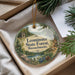 A round ornament with a scenic forest landscape and text, hanging from a string.