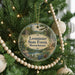 A circular ornament hanging on a Christmas tree, featuring a scenic landscape with a lake and pine trees.