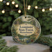 A circular ornament with a scenic forest landscape and text, hanging on a string.
