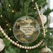 A round ornament hanging on a Christmas tree, featuring a scenic landscape with a cabin and a deer in the background.