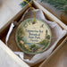 A round ornament with a tropical scene and a lighthouse, placed in a box with a white tissue paper lining.