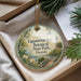 A round ornament with a tropical scene and a lighthouse in the background, placed in a box with pine branches.