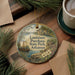 A decorative ornament with a painting of a river and a sailboat, surrounded by pine branches and a cup of coffee on a wooden surface.