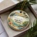 A decorative ornament in a box, featuring a tropical beach scene with palm trees, a bird, and a flower.