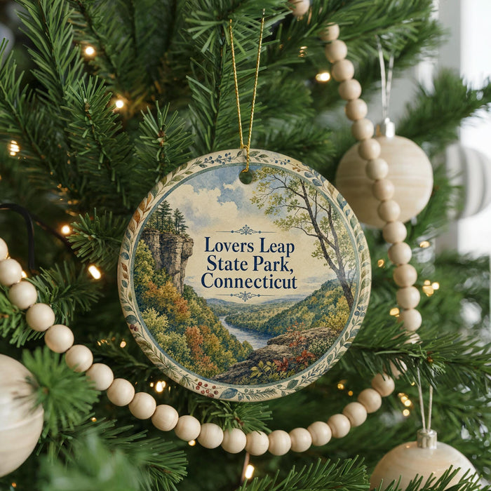 A round ornament hanging on a Christmas tree, featuring a scenic landscape with a river and mountains.