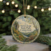 A round ornament with a scenic landscape of a river and mountains, surrounded by greenery, is displayed in front of a blurred background with twinkling lights.