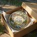 A decorative ornament in a box, featuring a scenic image of Lowell Heritage State Park in Massachusetts.